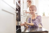 Smiling woman baking, placing cake in oven — Stock Photo