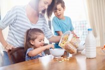 Mãe derramando cereal para filha na mesa de café da manhã — Fotografia de Stock