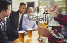 Bartender pouring beer from tap behind bar — Stock Photo