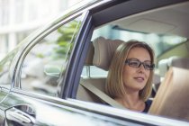 Geschäftsfrau liest Zeitung auf dem Rücksitz ihres Autos — Stockfoto