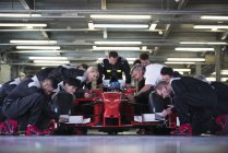 Pit crew preparing formula one race car and driver in repair garage — Stock Photo
