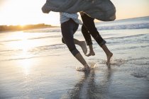 Ноги молодої пари біжать на пляжі на заході сонця — стокове фото