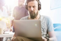 Serious male design professional with headphones using laptop in office — Stock Photo