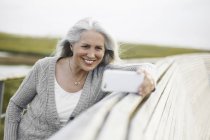 Усміхнена старша жінка бере селфі на прогулянковому виступі — стокове фото
