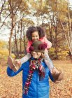 Retrato juguetona hija tirando de media gorra sobre los ojos de los padres en el parque de otoño - foto de stock