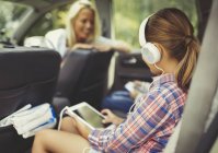 Chica con auriculares usando tableta digital viendo vídeo en el asiento trasero del coche - foto de stock