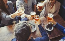 Vista aérea amigos comemorando, brindando cerveja e copos de vinho à mesa no bar — Fotografia de Stock