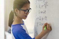 Portrait smiling, confident girl student solving physics equations at whiteboard in classroom — Stock Photo