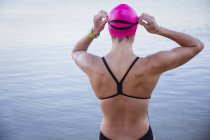 Rear view of open water swimmer adjusting swimming goggles at ocean — Stock Photo