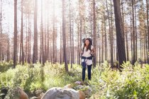 Smiling young woman with backpack hiking in sunny woods — Stock Photo
