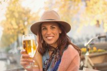 Portrait smiling young woman toasting beer glass at autumn sidewalk cafe — Stock Photo