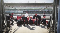 Manager and pit crew replacing tires on formula one race car in pit lane — Stock Photo