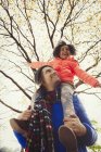 Father carrying enthusiastic daughter on shoulders below autumn tree in park — Stock Photo