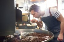 Asador de café masculino con olor a granos de café en el tostador - foto de stock