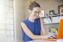 Retrato de mulher jovem com laptop laranja trabalhando no escritório em casa — Fotografia de Stock