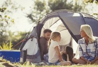 Family talking and relaxing outside tent at sunny campsite — Stock Photo