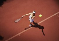 Vue aérienne jeune joueuse de tennis jouant au tennis, servant la balle sur un court de tennis ensoleillé en terre battue — Photo de stock