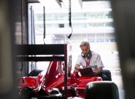 Manager mit Klemmbrett begutachtet Formel-1-Rennwagen in Werkstatt — Stockfoto