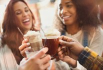 Amigos sonrientes brindando batidos y tazas de café en la cafetería - foto de stock