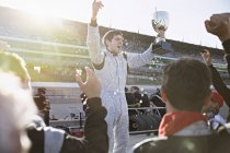 Equipe de Fórmula 1 torcendo pelo piloto com troféu, comemorando a vitória na pista de esportes — Fotografia de Stock