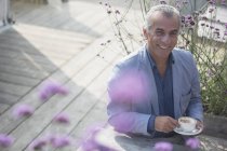 Портрет усміхнений старший чоловік п'є каву на сонячному патіо — стокове фото