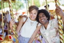 Young multiracial couple smiling on carousel in amusement park — Stock Photo
