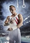 Male gymnast wrapping wrists below gymnastics rings in arena — Stock Photo