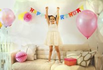 Retrato menina confiante com os braços levantados no sofá na festa de aniversário — Fotografia de Stock