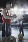 Trainer beobachtet männlichen Gewichtheber beim Auftragen von Kreidepuder auf die Hände an der Langhantel — Stockfoto