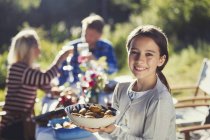 Portrait smiling girl serving food at sunny garden party patio table — Stock Photo