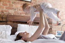 Mutter hebt Baby-Tochter kopfüber auf Bett — Stockfoto
