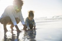 Mother and daughter crouching on beach and touching water — Stock Photo