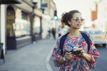 Молода жінка-туристка в сонцезахисних окулярах з камерою на міській вулиці — стокове фото