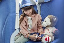 Girl fastening seat belt on stuffed animal on airplane — Stock Photo