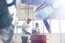 Mécanique de l'avion avec presse-papiers parlant à la boîte à outils dans le hangar — Photo de stock