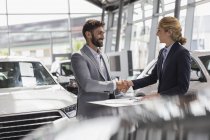 Car saleswoman and male customer handshaking in car dealership showroom — Stock Photo