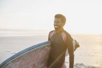 Surfeur masculin souriant marchant avec planche de surf sur la plage ensoleillée d'été — Photo de stock