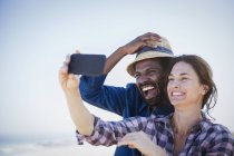 Riéndose, entusiasta pareja multiétnica tomando selfie con el teléfono de la cámara - foto de stock