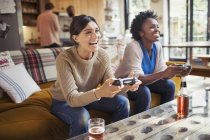 Laughing women friends playing video game on living room sofa — Stock Photo