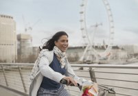 Entusiástico, sorridente mulher de bicicleta andando na ponte perto Millennium Wheel, Londres, Reino Unido — Fotografia de Stock