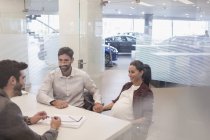 Продавець автомобілів розмовляє з вагітною парою в офісі автосалону — стокове фото