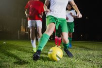 Junge Fußballspielerinnen, die nachts auf dem Feld spielen und gegen den Ball treten — Stockfoto