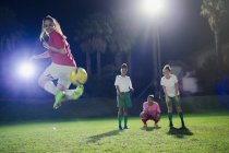 Jovens jogadoras de futebol praticando em campo à noite, fazendo chute de volta — Fotografia de Stock