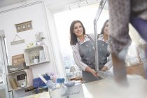 Smiling female artists moving painted mirror in art class workshop — Stock Photo
