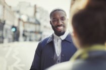 Усміхнений бізнесмен говорить з другом на сонячній міській вулиці — стокове фото