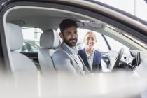 Portrait smiling, confident car saleswoman and male customer in driver?s set of new car in car dealership — Stock Photo