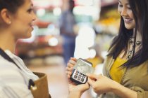 Female customer with credit card using contactless payment in store — Stock Photo