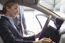 Lächelnde Frau beim Stöbern im neuen Auto, auf dem Fahrersitz im Autohaus — Stockfoto