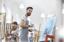 Retrato confiado artista masculino pintura con paleta en estudio de clase de arte - foto de stock