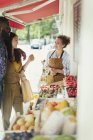 Trabajadora ayudando a pareja joven a comprar fruta en la tienda del mercado - foto de stock